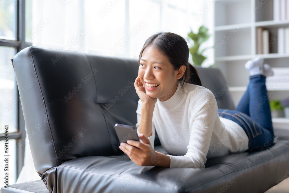 Beautiful young smiling Asian woman using smartphone on sofa at home. Beautiful young smiling Asian woman using smartphone on sofa at home.