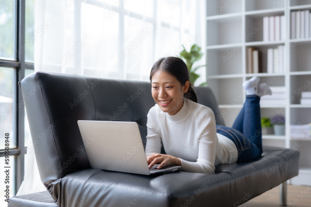 Happy young Asian woman relaxing using laptop computer on sofa at home. Happy young Asian woman relaxing using laptop computer on sofa at home.