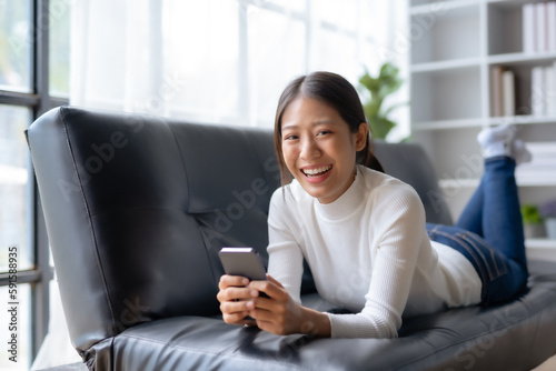 Beautiful young smiling Asian woman using smartphone on sofa at home.