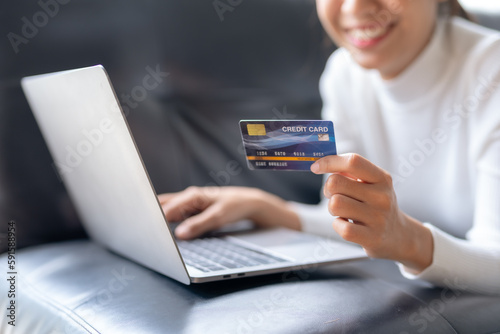 Happy young Asian woman using laptop computer and credit card for online shopping on sofa at home.