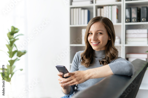 Beautiful young smiling woman using smartphone sitting on sofa at home.