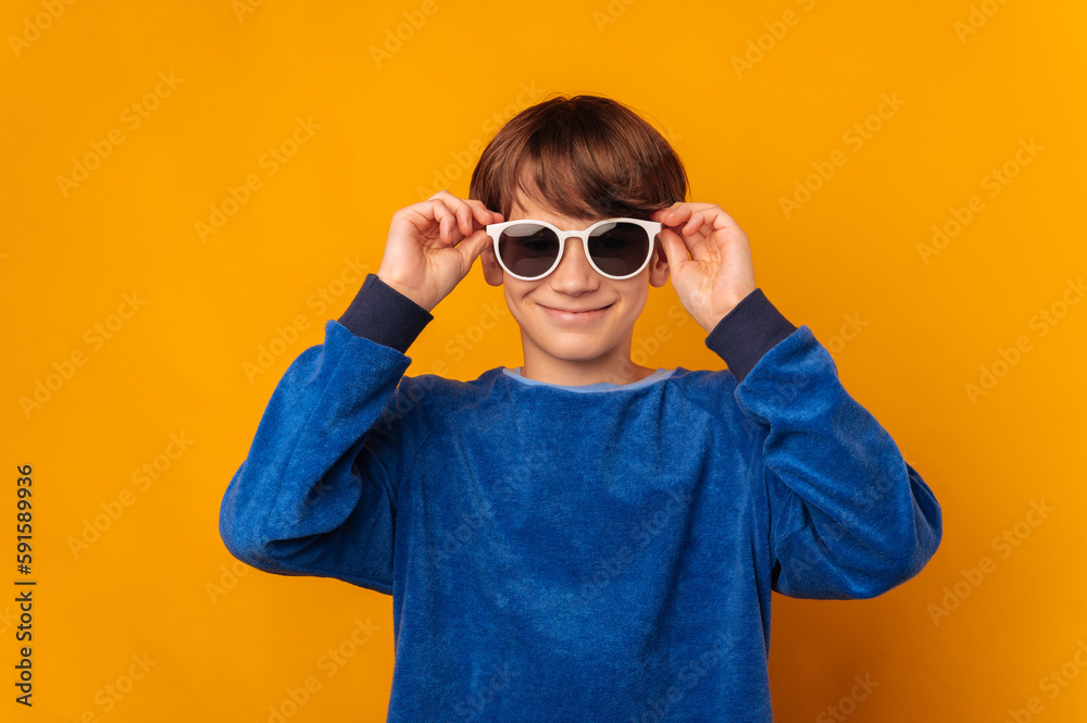 Studio portrait of a cool smiling teen boy putting on some sunglasses over yellow background. Studio portrait of a cool smiling teen boy putting on some sunglasses over yellow background.