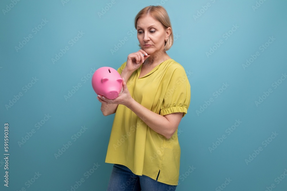 pensive blond middle-aged woman holding a piggy bank in her hands pensive blond middle-aged woman holding a piggy bank in her hands