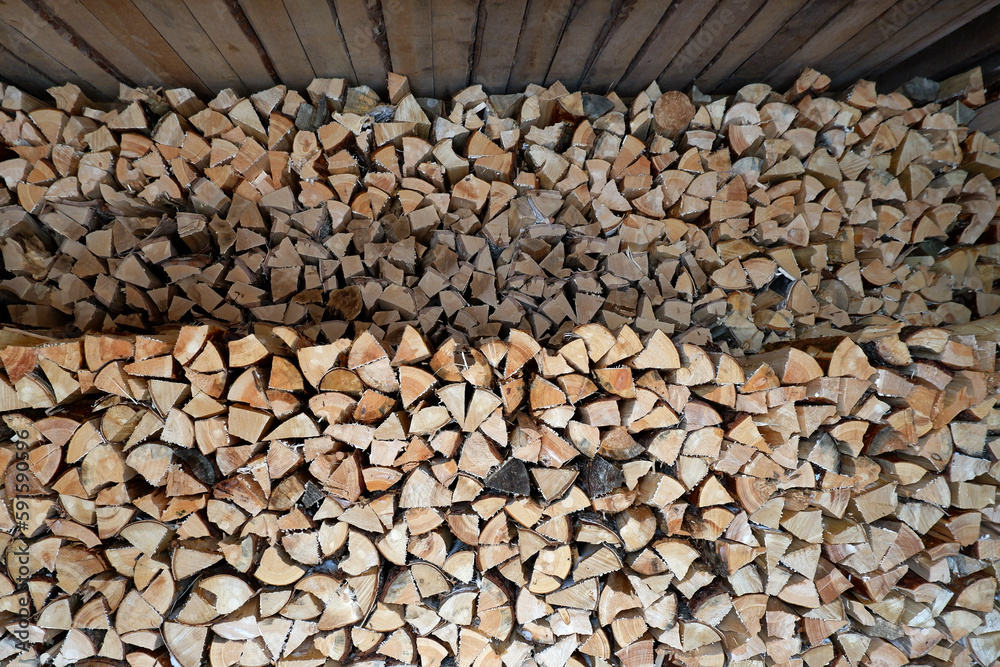 A pile of chopped wood stacked in two woodpiles under the roof. A lot of wood for a fire, burning in the oven.Buying and selling firewood for the winter. Storage and drying of firewood