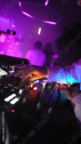Vertical Video, Unrecognizable DJ Creates Dynamic Atmosphere on Dance Floor with Classic, Modern, and Remixed Tracks and Music, Mixing with Turntables in Nightclub and Neon Lighting. Slow motion