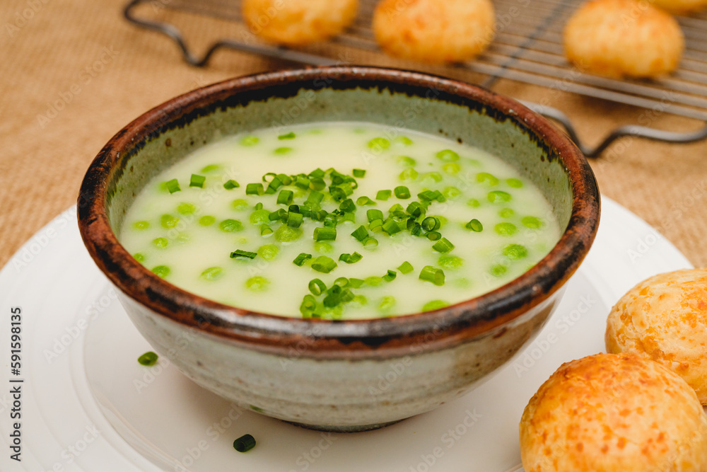 Celery cream soup with a green pea in a bowl garnished with chopped green onion and served with freshly baked cheese bread close-up