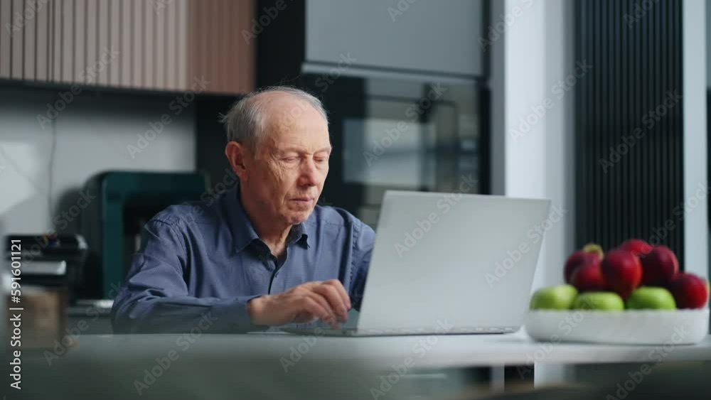 Healthy Elderly Man Using Modern Laptop, Sitting Alone In Home Kitchen, Typing Text On Keyboard Healthy Elderly Man Using Modern Laptop, Sitting Alone In Home Kitchen, Typing Text On Keyboard