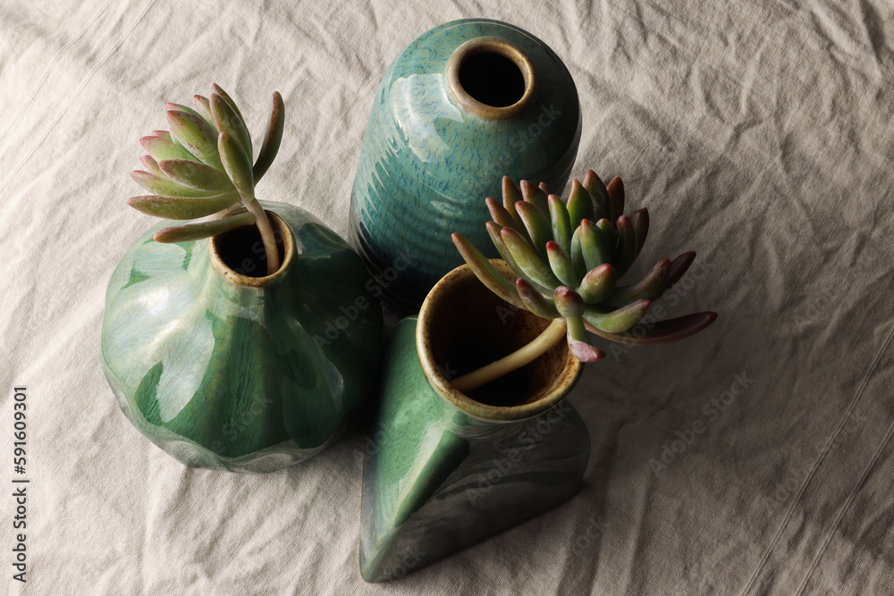 Piccoli vasi in ceramica di colore verde, blu e azzurro, composizione vista dall’alto su un fondo di tela di lino