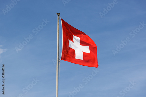 swiss flag in the wind in front of a blue sky sunshine during the day. light veil clouds. direct democracy and freedom. sunshine during the day without people