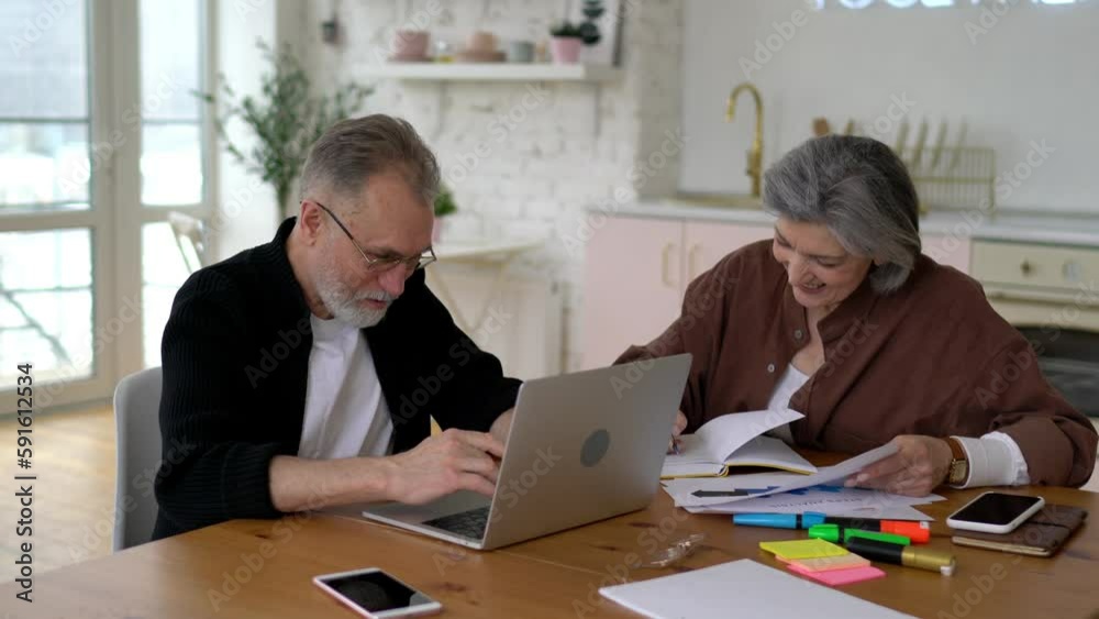 Caucasian mature couple collaborating on startup project during weekend time in home interior, skilled adult male and female graphic designers with laptop computer browsing web page 
