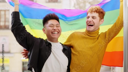 Excited gay couple waving a lgbt flag on the balcony