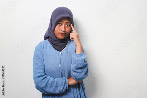 Pensive young Asian girl in hijab standing with fingers on chin