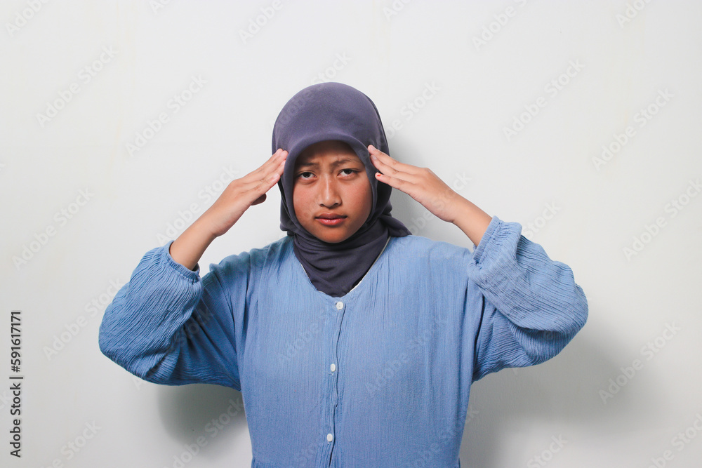 Young Asian girl in hijab grabbing her head while thinking about something Young Asian girl in hijab grabbing her head while thinking about something