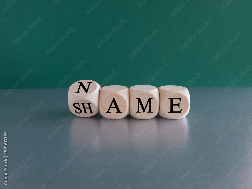 Name or shame symbol. Turned the wooden cube and changes the concept word Shame to Name. Beautiful gray table green background, copy space. Business, name or shame concept.