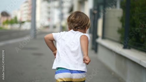 Back of happy kid walking outside in city street. Child standing in urban sidewalk © Marco