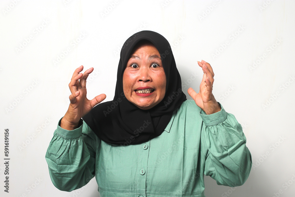 Angry Middle aged Asian women wearing hijab raised her hand while looking at camera Angry Middle aged Asian women wearing hijab raised her hand while looking at camera