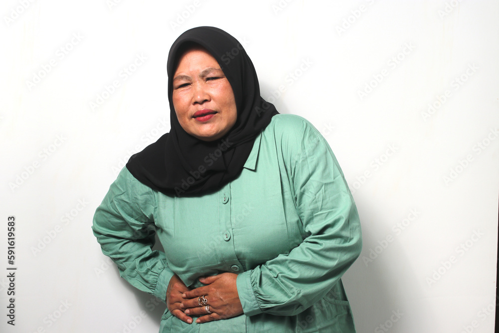 Unhealthy Middle aged Asian women wearing black hijab and green casual shirt, feels so sick suffering From Acute Abdominal, Menstrual Pain Or Problems With Digestion isolated on white background. Unhealthy Middle aged Asian women wearing black hijab and green casual shirt, feels so sick suffering From Acute Abdominal, Menstrual Pain Or Problems With Digestion isolated on white background.