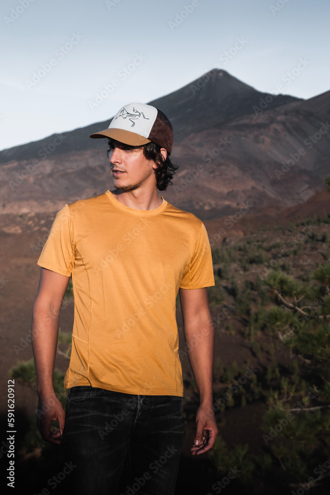 Young man with long hair and sun trucker cap with yellow shirt in a mountain landscape at the sunset in tenerife. With the Teide peak in the background. Young man with long hair and sun trucker cap with yellow shirt in a mountain landscape at the sunset in tenerife. With the Teide peak in the background.