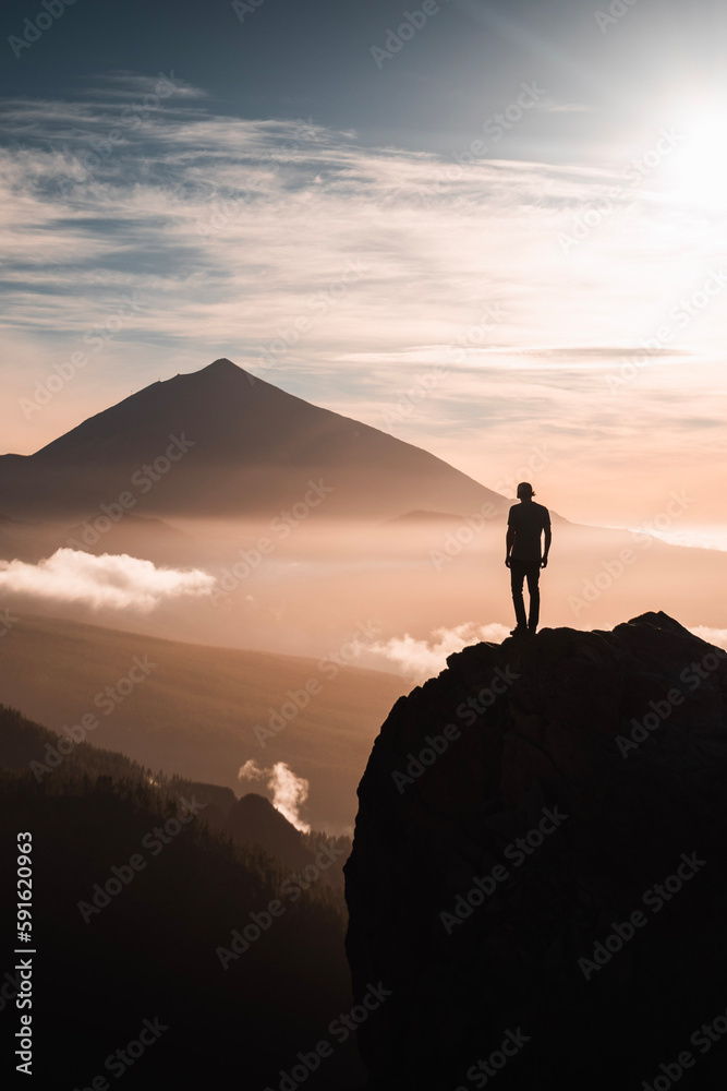 Silhouette of a man standing on a rock observing the landscape of Teide peak at sunset in backlight.