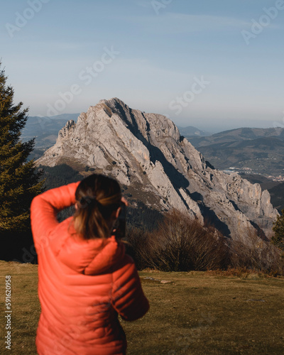 Girl photographer in winter clothes taking a picture of a mountainous landscape in the Urkiola area, near Anboto, in the Basque Country.