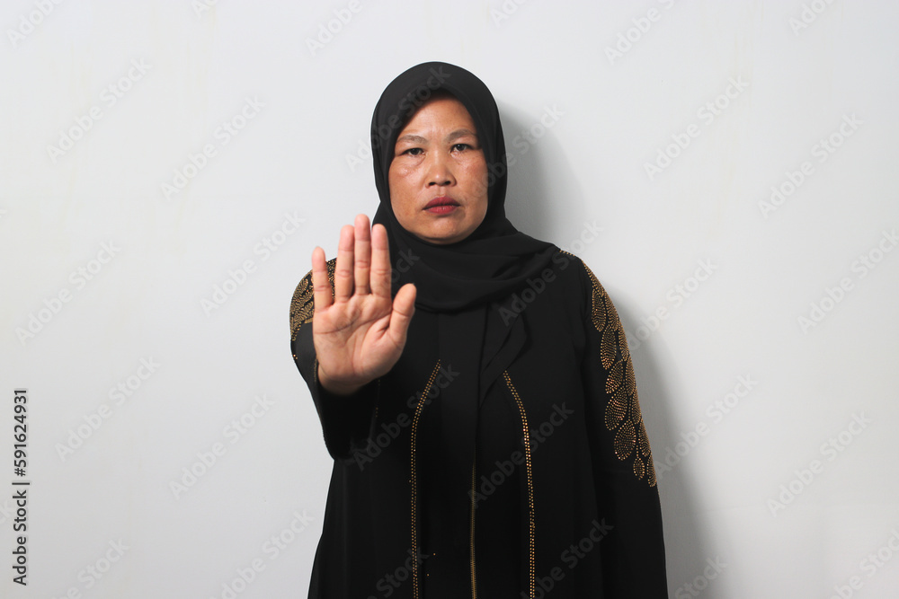 Serious Middle aged Asian women wearing hijab standing with outstretched hand showing stop gesture Serious Middle aged Asian women wearing hijab standing with outstretched hand showing stop gesture