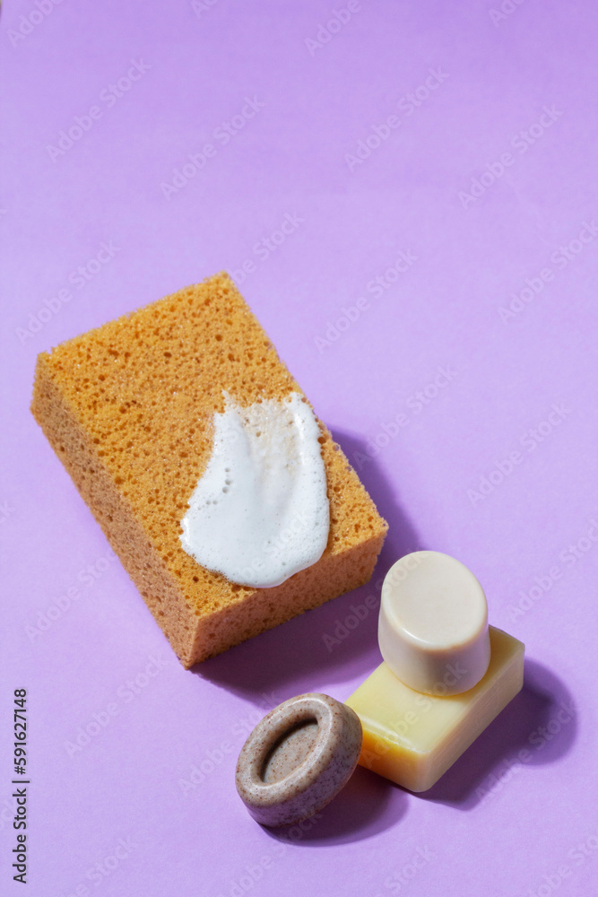 Handmade soap with the addition of coffee and wild herbs and a sponge with foam on a purple background.