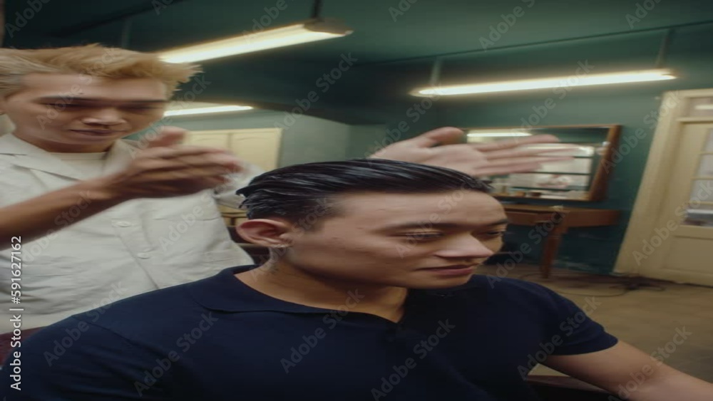 Young handsome Asian barber styling his hair and hair of male client after giving a haircut in the barbershop. Vertical format clip Young handsome Asian barber styling his hair and hair of male client after giving a haircut in the barbershop. Vertical format clip