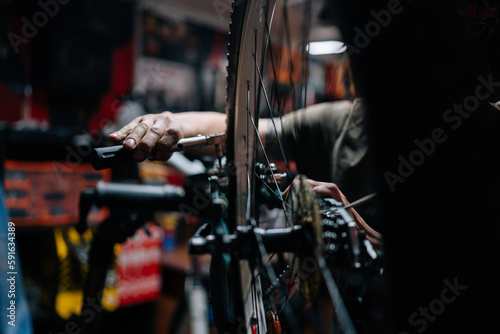 Close-up hands of unrecognizable repairman repairing mountain bike using special tool working in bicycle repair shop with dark interior. Concept of professional repair and maintenance of bicycle.