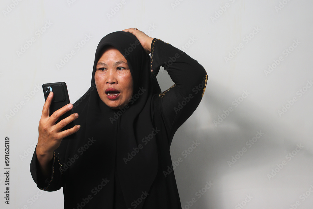 Middle aged Asian women wearing hijab feels sad reading bad news on mobile phone Middle aged Asian women wearing hijab feels sad reading bad news on mobile phone
