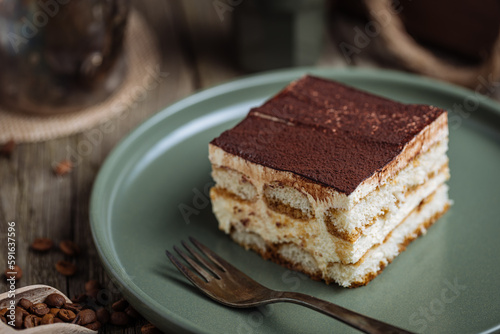 A piece of Tiramisu cake, traditional Italian dessert, served in moody, rustic scene. Wooden background and green plate. 