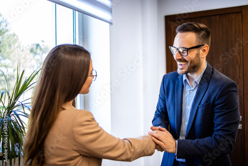 Man in business suit shaking hands and welcoming new female colleague in the office.