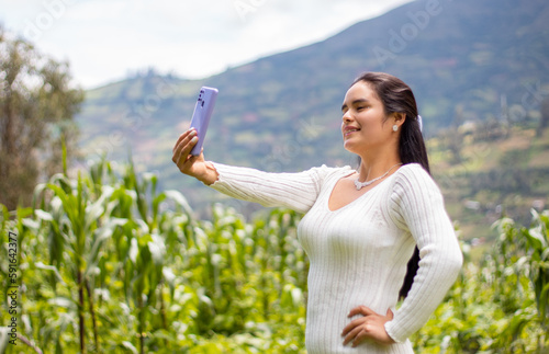 Chica hermosa parada junto al campo en las montañas y tomando selfies