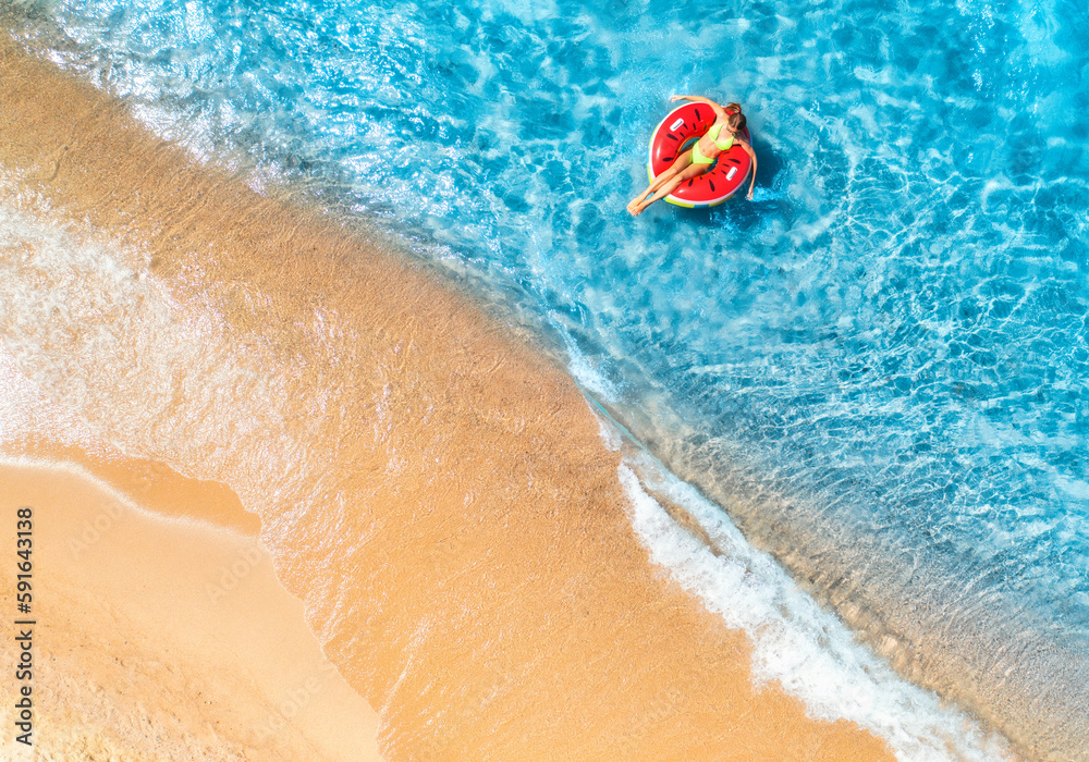 Fototapeta premium Aerial view of a young woman swimming with red swim ring in blue sea with waves at sunset in summer. Tropical landscape with girl, clear water, sandy beach. Top view. Vacation. Sardinia island, Italy