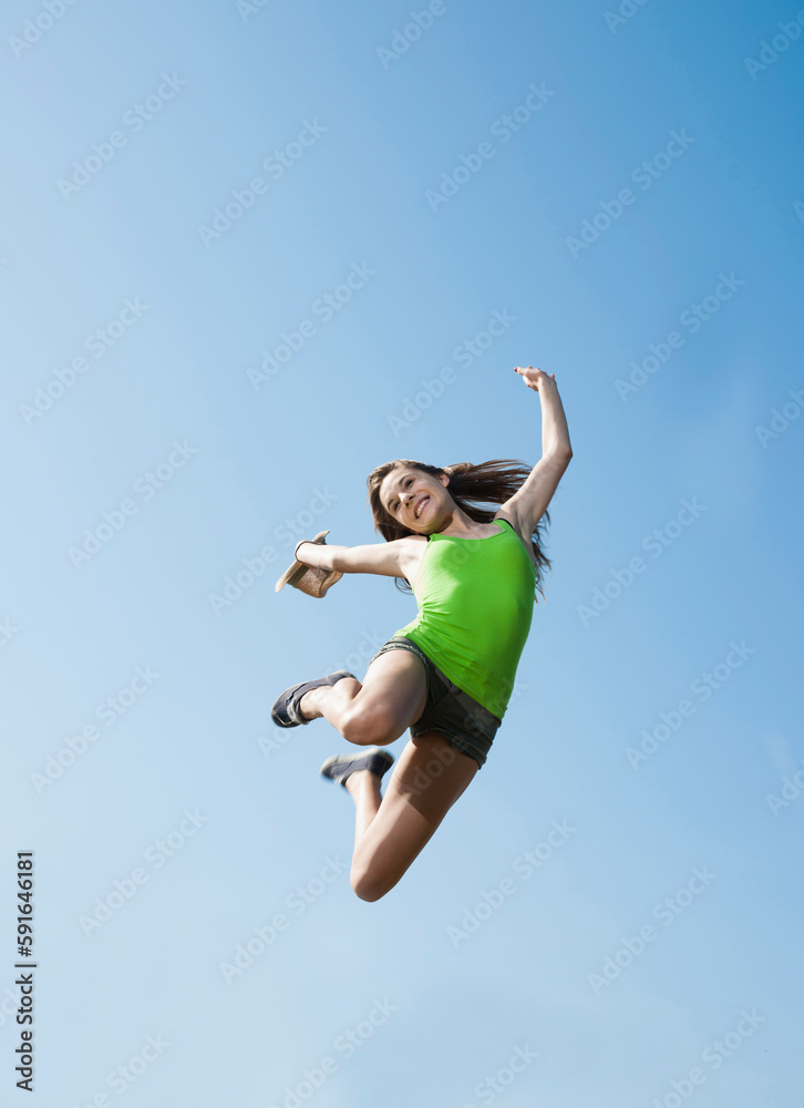 Teenaged girl jumping in mid-air against blue sky, Germany Teenaged girl jumping in mid-air against blue sky, Germany