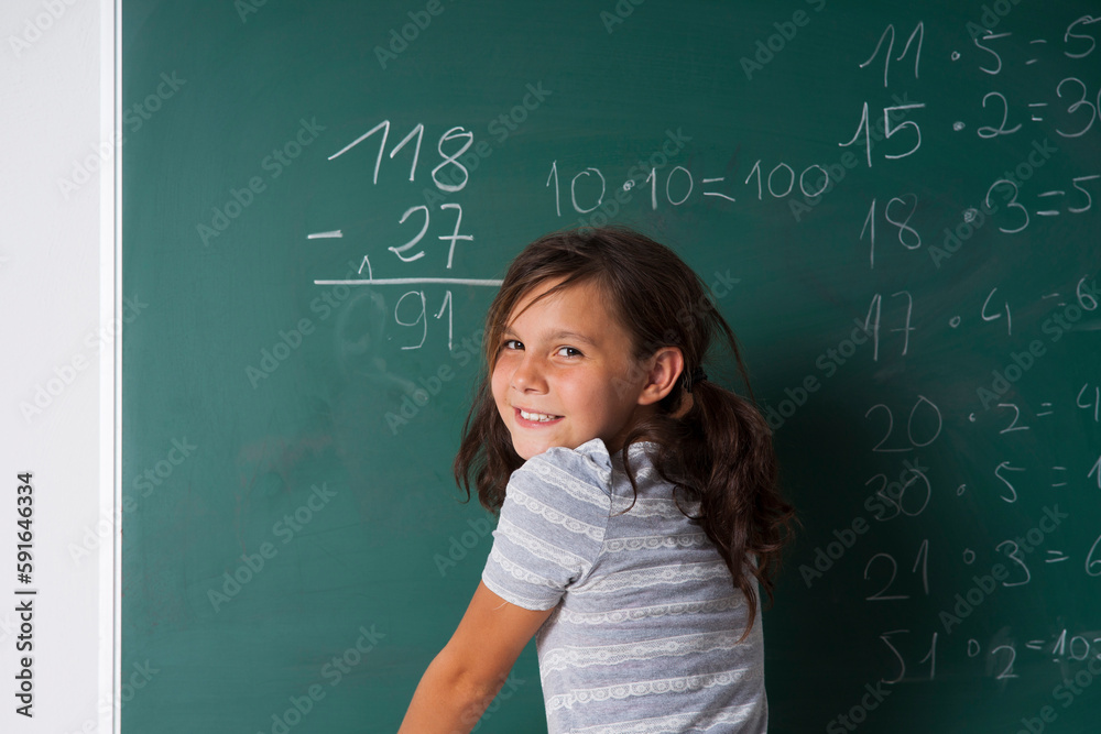 Girl standing in classroom in front of blackboard dong mathematical questions, Germany Girl standing in classroom in front of blackboard dong mathematical questions, Germany