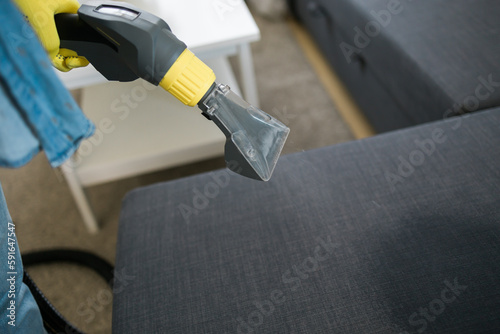 Man holding modern washing vacuum cleaner and cleaning dirty sofa with professionally detergent. Professional springclean at home concept photo