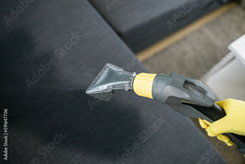 Man in protective rubber glove cleaning sofa with professionally extraction method with washing vacuum cleaner. Early spring regular cleanup. Commercial cleaning company concept