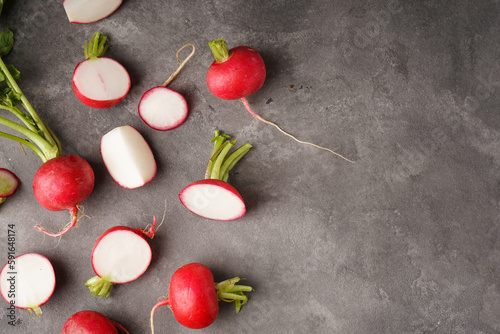 Fresh red radishes slice with leaves on grey background, space for text, flat lay.
