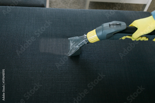 Man in protective rubber glove cleaning sofa with professionally extraction method with washing vacuum cleaner. Early spring regular cleanup. Commercial cleaning company concept