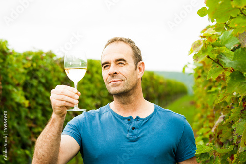 Close-up of vintner standing in vineyard, holding galss of wine and examining quality, Rhineland-Palatinate, Germany photo