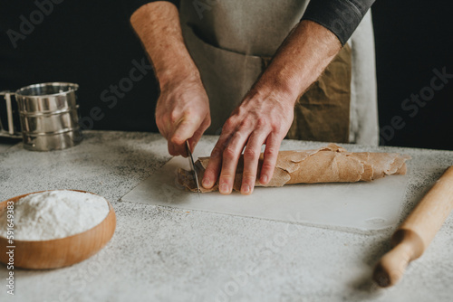 Unrecognizable man cutting the dough with a knife on a white background