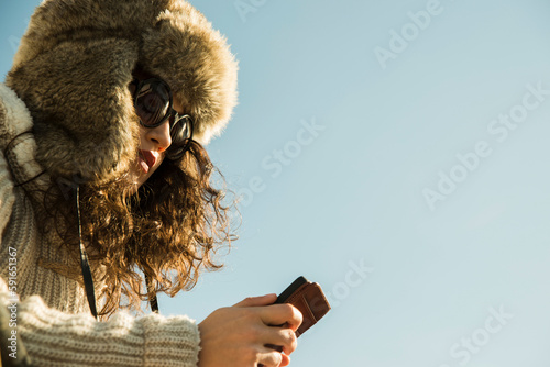 Close-up of teenage girl outdoors, wearing trapper hat and sunglasses, looking down at smart phone, Germany photo