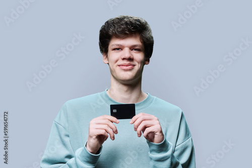 Young handsome guy holding credit card in hands on grey background © Valerii Honcharuk