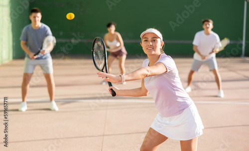 Concentrated young hispanic female frontenis player swinging string racquet to hit ball on outdoor three-walled court on sunny summer day. Sport and active lifestyle concept.. © JackF
