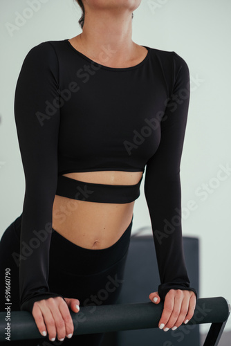 Unrecognizable woman wearing black sportswear practicing pilates exercises on reformer machine in studio.