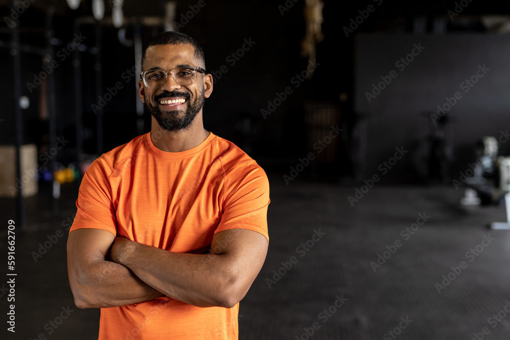 Portrait of bearded biracial young man with arms crossed smiling and standing in gym Portrait of bearded biracial young man with arms crossed smiling and standing in gym