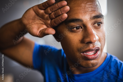 Closeup of tired biracial young man wiping sweat from forehead while exercising in gym photo
