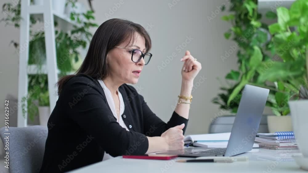 Serious talking mature woman at home office using laptop for video call chat Serious talking mature woman at home office using laptop for video call chat