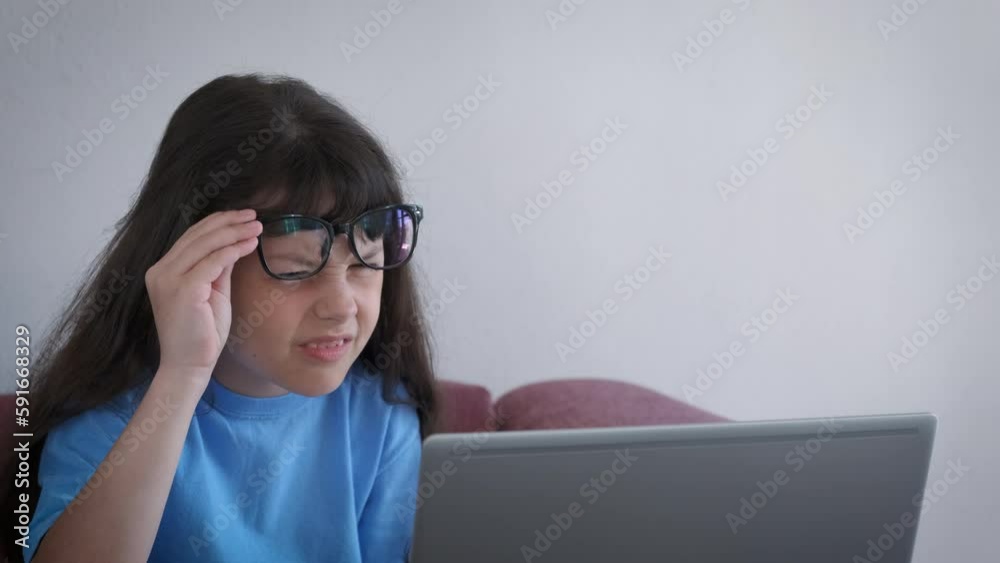 Child with glasses squinting eyes by laptop. A stressed little girl wear glasses for better vision by her laptop. A concept of eyes trouble because of computer working at home. Child with glasses squinting eyes by laptop. A stressed little girl wear glasses for better vision by her laptop. A concept of eyes trouble because of computer working at home.