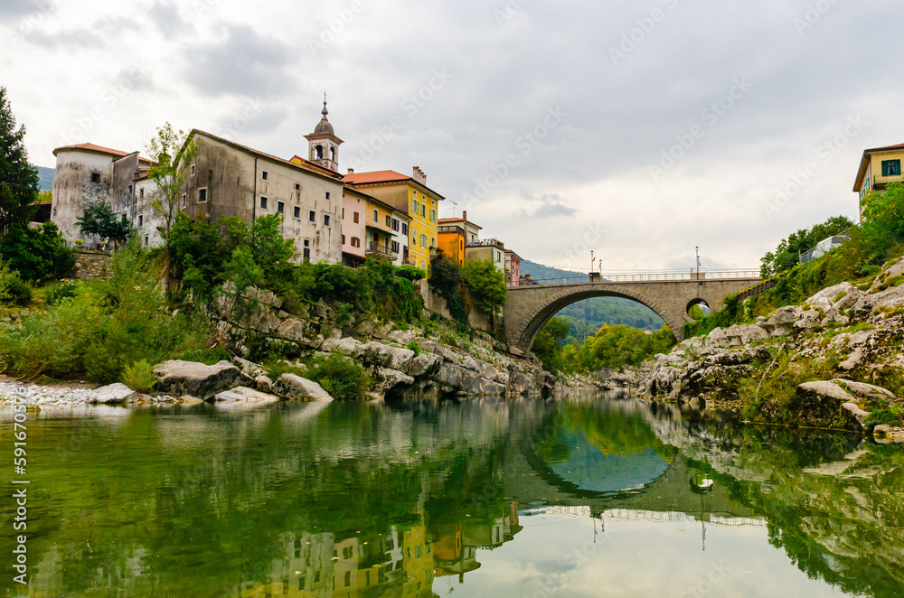 River Soca in Slovenia - Kanal ob Soči city with a beautiful old stone arch bridge and reflection in water. 